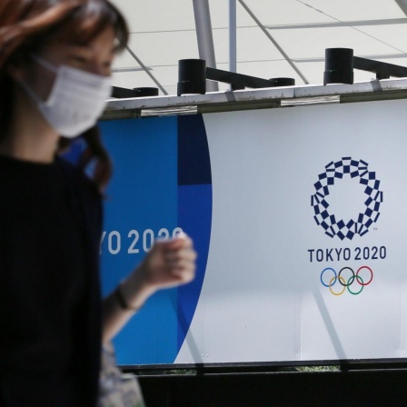 Eine Japanerin mit Mundschutz läuft an den Loos der Olympischen und Paralympischen Spielen in Tokio vorbei