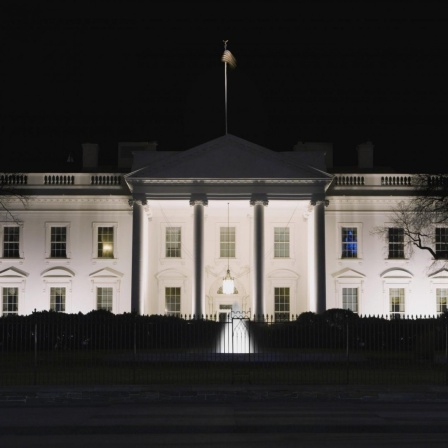 Das White House in Washington DC bei Nacht, in einem Fenster scheint Licht.