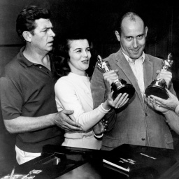 Vier Personen stehen neben dem Filmkomponisten Henry Mancini, der zwei Oscar-Trophäen in den Händen hält.