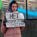 Eine Demonstrantin protestiert mit einem selbst gemalten Schild in Moskau gegen den Krieg in der Ukraine. Die junge Frau mit rosa Mantel hält das Papier vor sich.