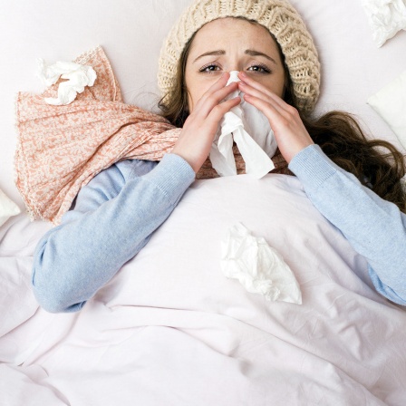 Symbolbild Erkältung - Eine Frau liegt schniefend und triefend im Bett.