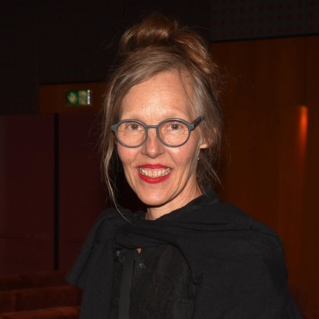 Porträt von Donata Wenders vor dunklem Hintergrund. Sie lacht in die Kamera.