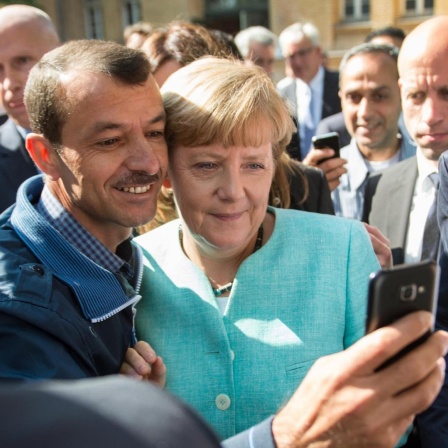 Bundeskanzlerin Angela Merkel (CDU) lässt sich am 10.09.2015 nach dem Besuch einer Erstaufnahmeeinrichtung für Asylbewerber der Arbeiterwohlfahrt (AWO) und der Außenstelle des Bundesamtes für Migration und Flüchtlinge in Berlin-Spandau für ein Selfie zusammen mit einem Flüchtling fotografieren. Foto: Bernd von Jutrczenka/dpa