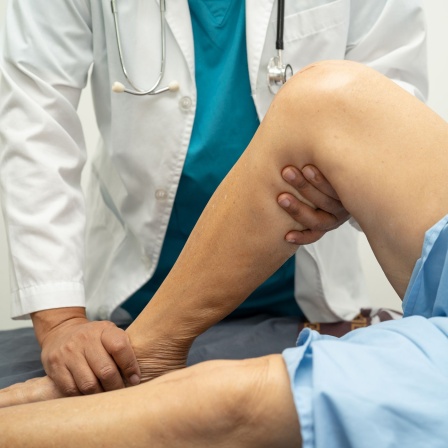 Arzt untersucht das Knie einer älteren Frau