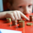 Ein fünfjähriger Junge sitzt an einem roten Tisch und zählt sein gespartes Taschengeld