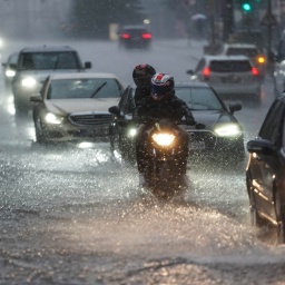 Autos und Motorräder fahren bei starkem Regen über die überflutete Friedrichstraße in Berlin-Mitte.