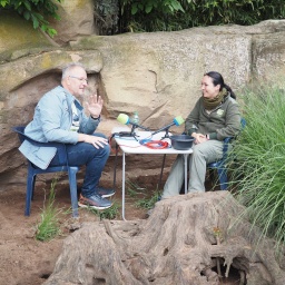 Ein Mann und eine Frau sitzen neben einem Felsen an einem Tisch mit Mikrofonen.