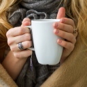 Eine Frau wärmt sich in eine Decke gehüllt, an einer Tasse Tee in den Händen