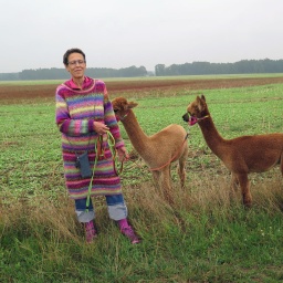 Schirin Schahbaz posiert mit zwei ihrer Alpakas auf einem Feld für ein Foto.