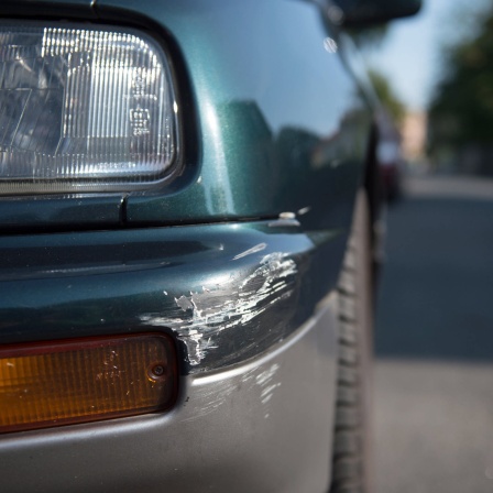 An der Ecke eines Front-Stoßfängers eines geparkten Autos sind Spuren eines Unfalls zu sehen.