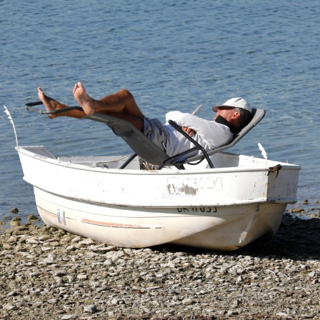 Weil der Liegestuhl auf dem steinigen Untergrund wackelt, hat der Mann diesen in das am Ufer liegende Boot gestellt.