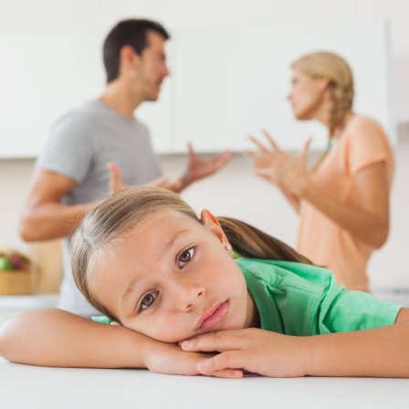Ein Mädchen ist traurig, im Hintergrund streiten die Eltern. Kinder lernen Verhaltensmuster in der Kindheit. Diese prägen, wie sie zum Beispiel später mit Konfliktsitutionen umgehen.