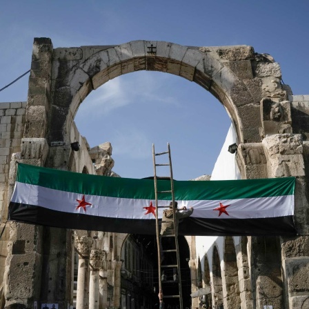 Ein Arbeiter hängt eine Flagge der syrischen Revolutionäre - grün, weiß, schwarz mit roten Sternen am Eingang zu dem Suq al-Hamidiya, vor dem Freitagsgebet auf.