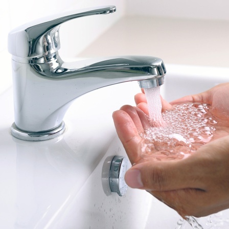Hände unter einem aus einem Wasserhahn sprudelnden Wasserstrahl
