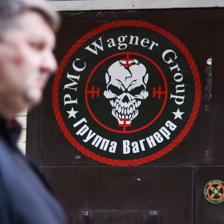 Ein Mann geht an einer Tür vorbei, auf der ein Logo der Gruppe Wagner zu sehen ist. 