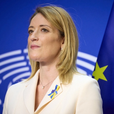 Ein Porträtbild zeigt die Präsidentin des Europäischen Parlaments, Roberta Metsola, mit EU-Fahne und Parlamentslogo im Hintergrund.