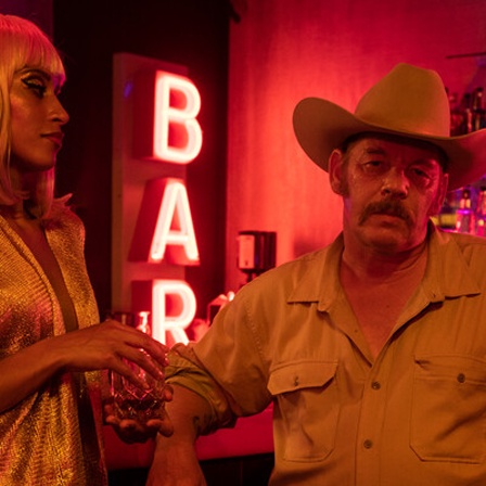 Eine Szene aus der Serie "Boom Boom Bruno": Ben Becker als Bruno und Sabrina Ceesay als Alice stehen am Tresen in einer Bar mit rotem Licht.