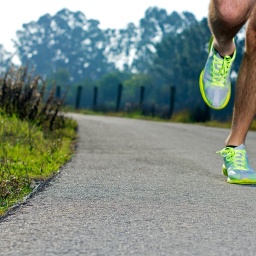 Läufer mit neongelben Sportschuhen trainiert auf asphaltiertem Weg