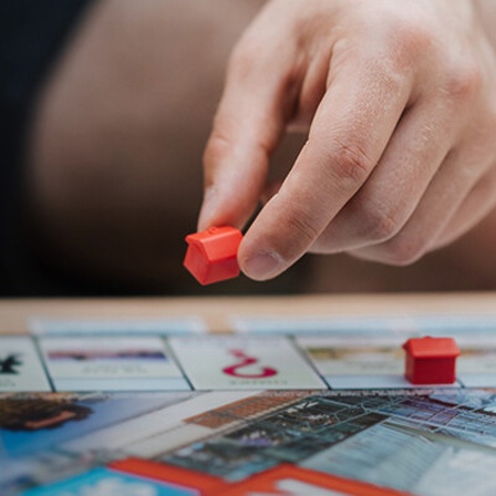 Eine Hand versetzt ein Spielhaus auf einem Monopoly-Spielbrett.