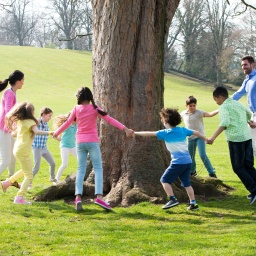 Kinder tanzen um einen Baum