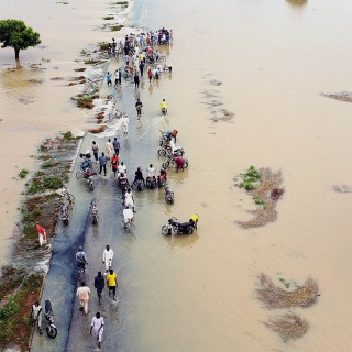 Menschen in Nigeria gehen nach heftigen Regenfällen über eine teils überschwemmte Straße. 