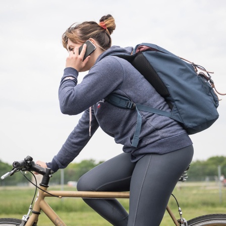 Eine Frau fährt mit dem Fahrrad auf dem Tempelhofer Feld in Berlin und telefoniert mit einem Smartphone (gestellte Szene).