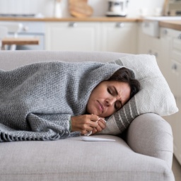 Eine Frau liegt, in eine Decke eingewickelt, auf dem Sofa.