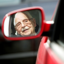 Ein älterer Mann fährt Auto und schaut dabei in den Rückspiegel