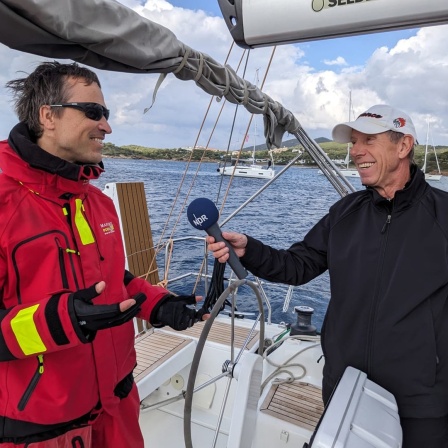 Ein lächelnder Reporter interviewed einen Skipper auf einer Jacht in der Ägäis