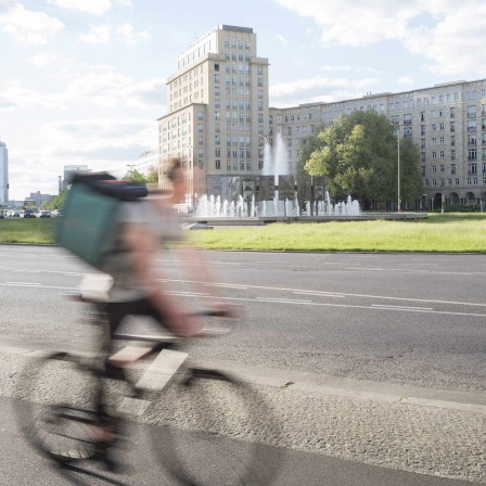 Ein Radfahrer fährt auf der Karl-Marx-Allee am Springbrunnen am Strausberger Platz vorbei. 