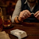 Männerhände, die eine Zigarette zerbrechen und daneben ein Glas mit einem alkoholischen Getränk. 