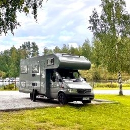 Ein Wohnmobil steht geparkt unter Birken auf einem Parkplatz in Finnland
