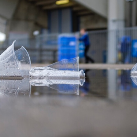 An einem Fußballstadion liegen kaputte Plastikbecher auf dem Boden.