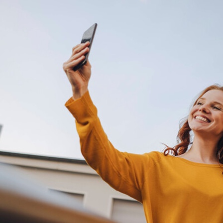 Eine Frau lächelt und winkt in ihr Smartphone.