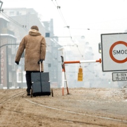 Eine Person zieht einen Koffer durch braunen Schnee neben einem Schild mit der Aufschirft "Smog-Alarn".