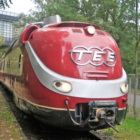 Ein Zug mit roter Lokomotive steht an einem Bahnsteig. Auf der Lokomotive steht in großen Buchstaben &quot;TEE&quot;.