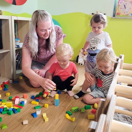 Eine Tagesmutter spielt mit drei Kleinkindern.