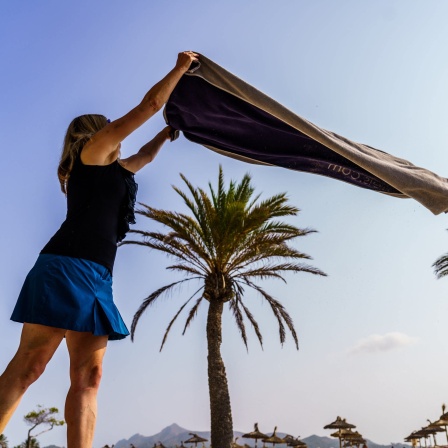 Eine Frau breitet am Strand ihr Handtuch aus. Endlich wieder Urlaub mit Strand und Pool.