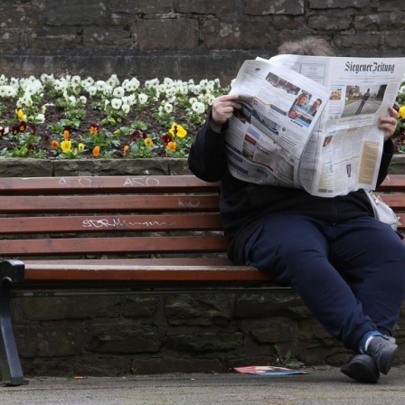 Eine Frau sitzt auf einer Bank und liest die "Siegener Zeitung".