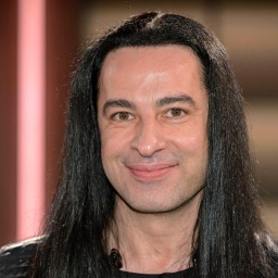 Der Comedian Bülent Ceylan mit langen, schwarzen Haaren lacht in die Kamera.