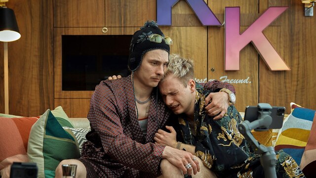 Szenenbild aus der Impro-Serie "Kranitz - Bei Trennung Geld zurück": Zwei Männer in bunt gemusterten Morgenmänteln sitzen auf einem Sofa und halten sich in den Armen.