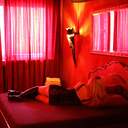 Eine mit Dessous bekleidete Frau liegt in einem rot beleuchtetem Zimmer auf einem Bett
