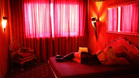 Eine mit Dessous bekleidete Frau liegt in einem rot beleuchtetem Zimmer auf einem Bett