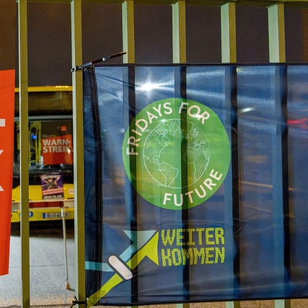 Ein Plakat mit der Aufschrift "ver.di - Heute Warnstreik" hängt neben einem Transparent der Klima-Bewegung "Fridays for Future" am Zaun eines Busbetriebshofs.