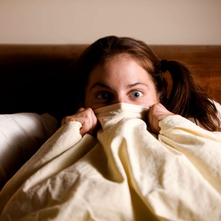 Frau im Bett zieht sich die Decke übers Gesicht