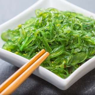 Das Bild zeigt das japanische Gericht Algensalat in einer weißen Schale mit Essstäbchen.