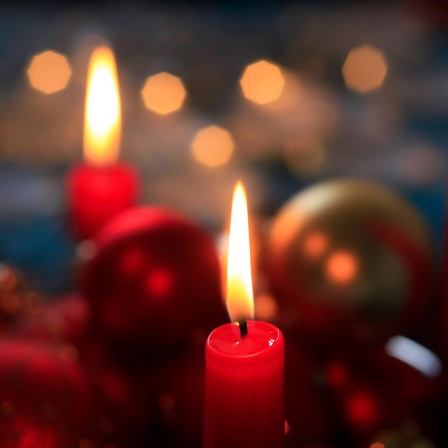 Rot brennende Adventskerzen und Christbaumkugeln.