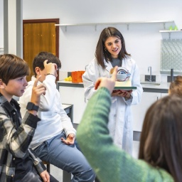Naturwissenschaftslehrer, der Oberstufenschülern die Anatomie des menschlichen Auges anhand eines Modells während einer Biologiestunde im Schullabor erklärt. Zwei Jungs und zwei Mädchen hören gespannt zu und melden sich.