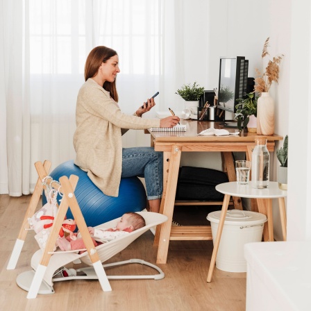 Eine Frau mit Smartphone sitzt an einem Arbeitsplatz.