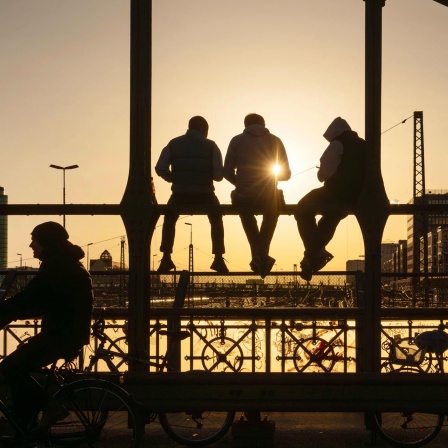 Jugendliche sitzen im Sonnenuntergang auf einer Brücke.